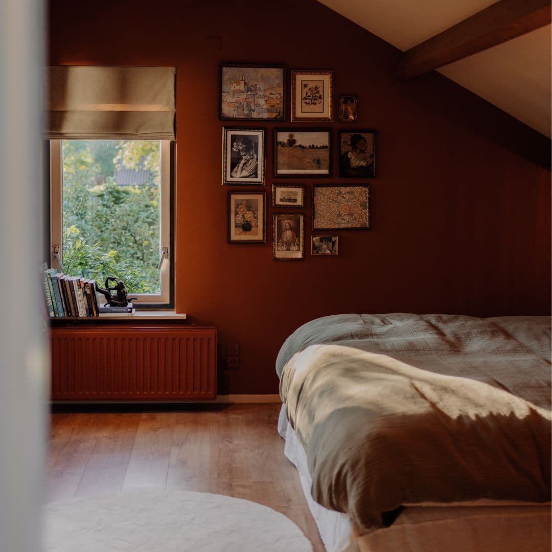 Bed en Breakfast Sauwerd 11 Sfeervolle slaapkamer met warme terra tinten, vintage gallery wall, boeken op de vensterbank en een opgemaakt bed.