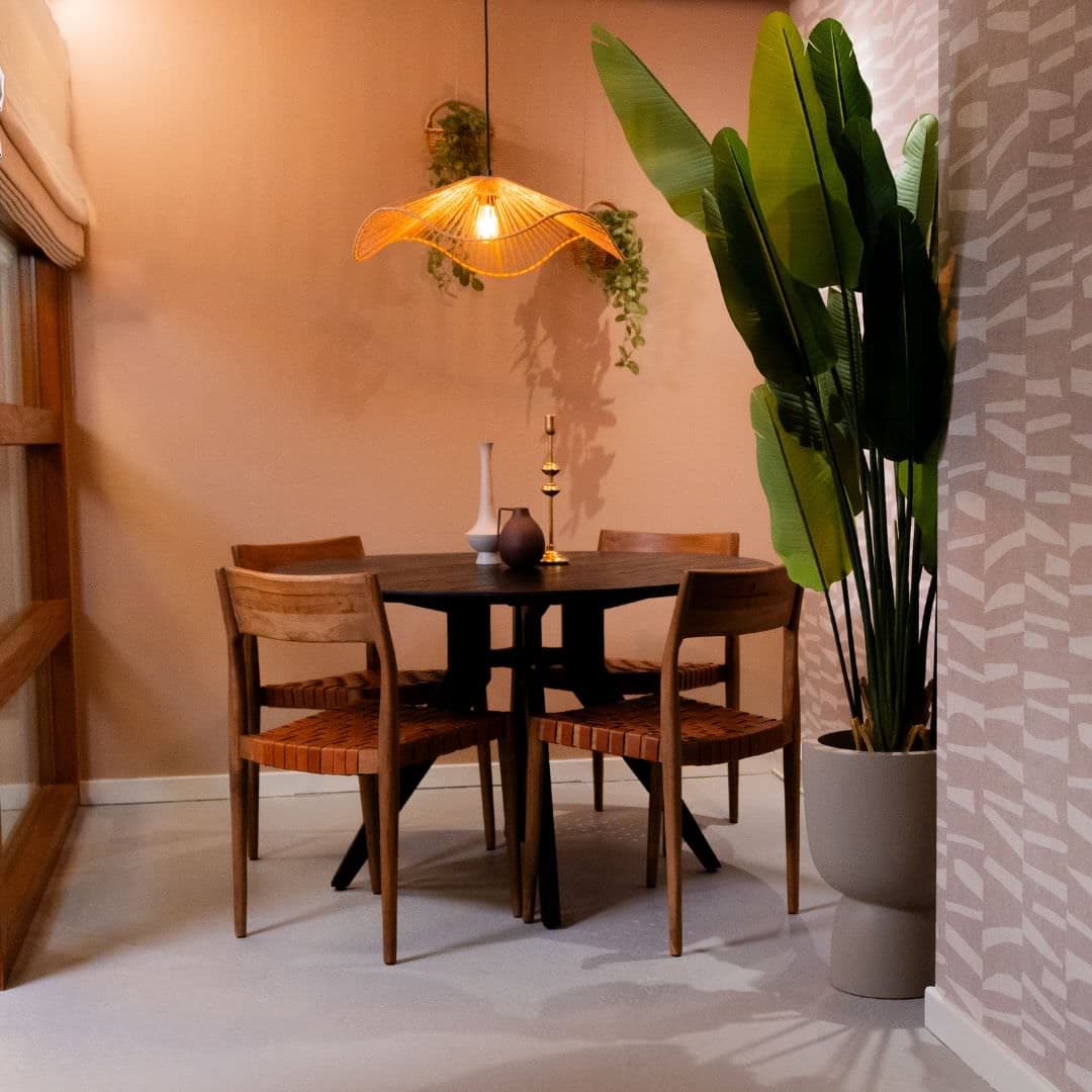 Warme en sfeervolle eetkamer en overlegruimte in bohemian stijl met aardse kleuren, een ronde eettafel, hout- en leder eetkamerstoelen, rotan hanglamp, vaasjes en kandelaar, kamerplanten, sfeervol behang en een moderne gietvloer.
